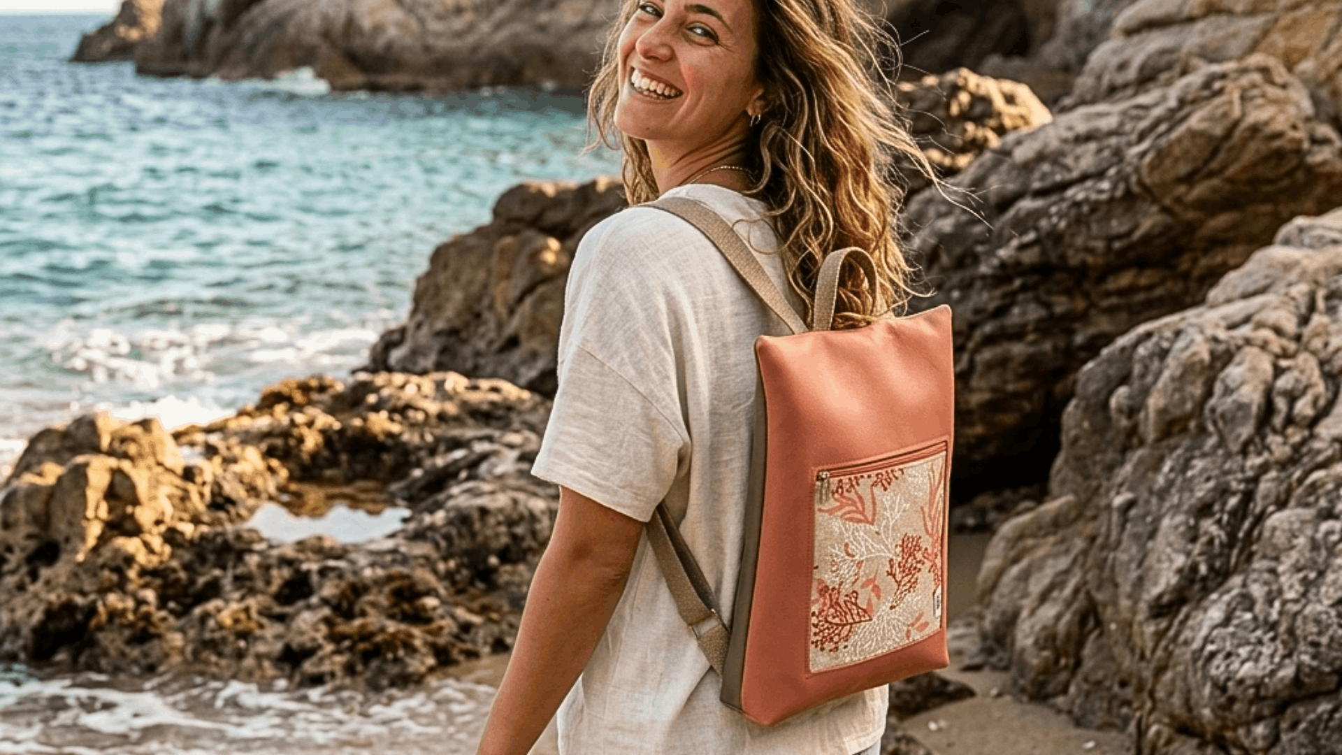 Mujer en la playa con mochila antirrobo color coral de Cristina Alba